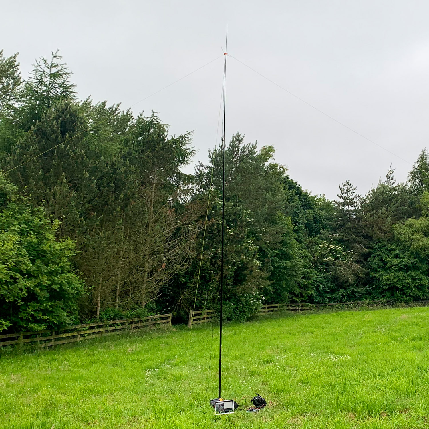 A picture of a 6m fibreglass pole, assorted radio equipment and laptop at the foot, and wires from the side